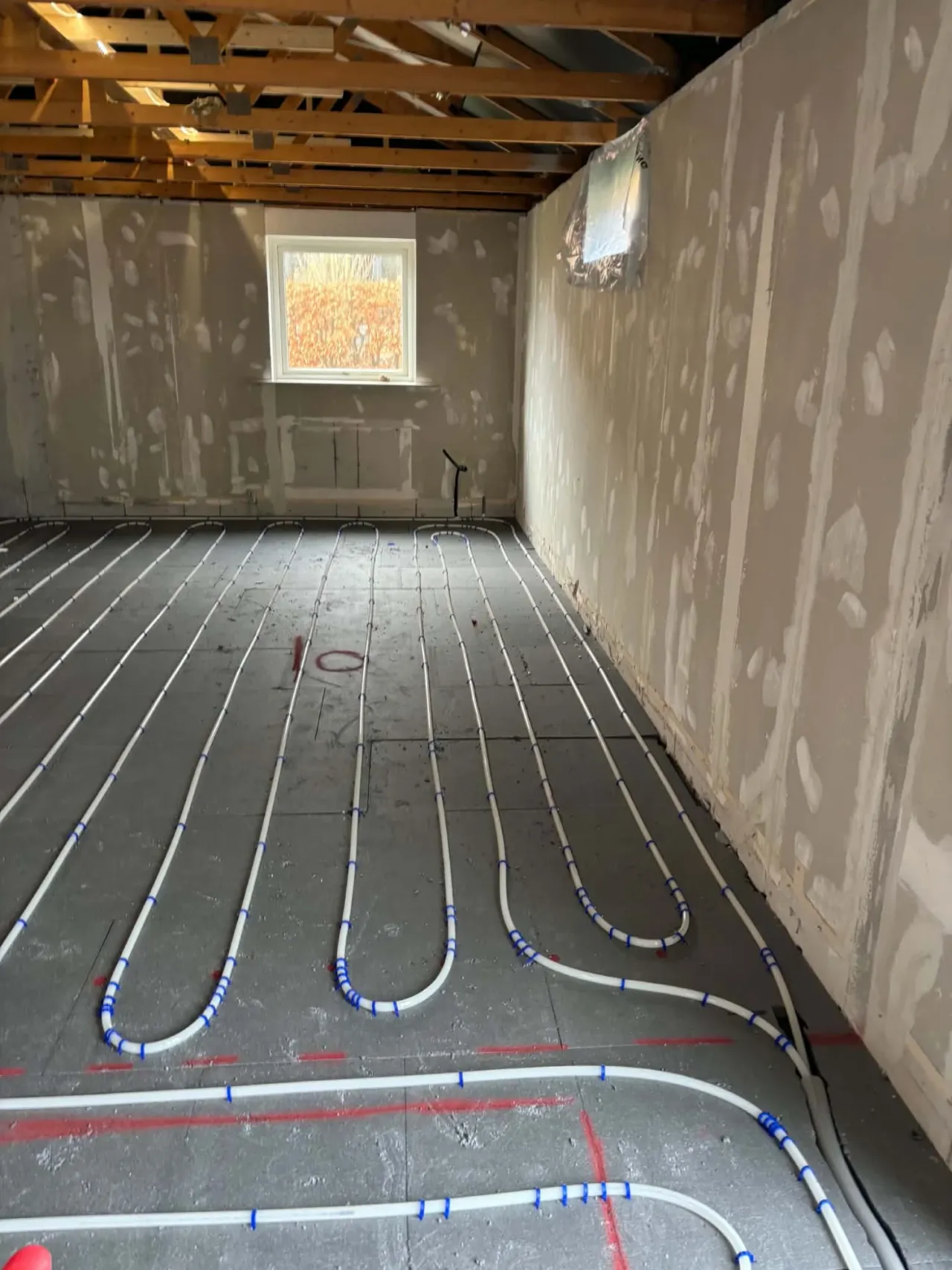 Gulvvarmerør lagt i sløjfer på isoleringsplader i et rum under renovering